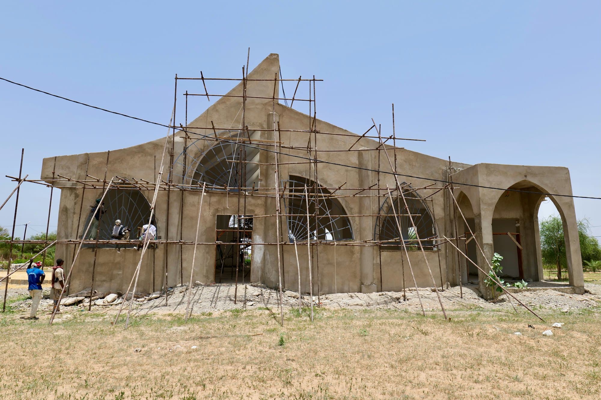 A building under construction with timber scaffolding, workers on site