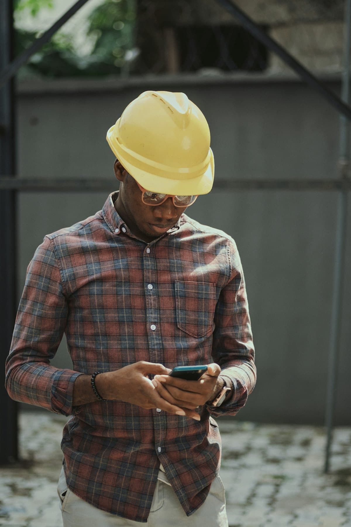 A man in a yellow hard hat checking his phone on site