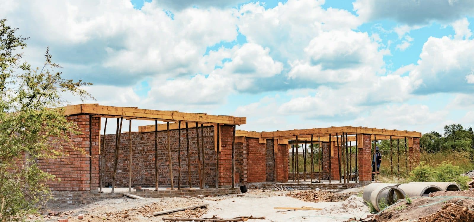 Timber roof trusses being fitted on the brick walls of a long single-story house under construction