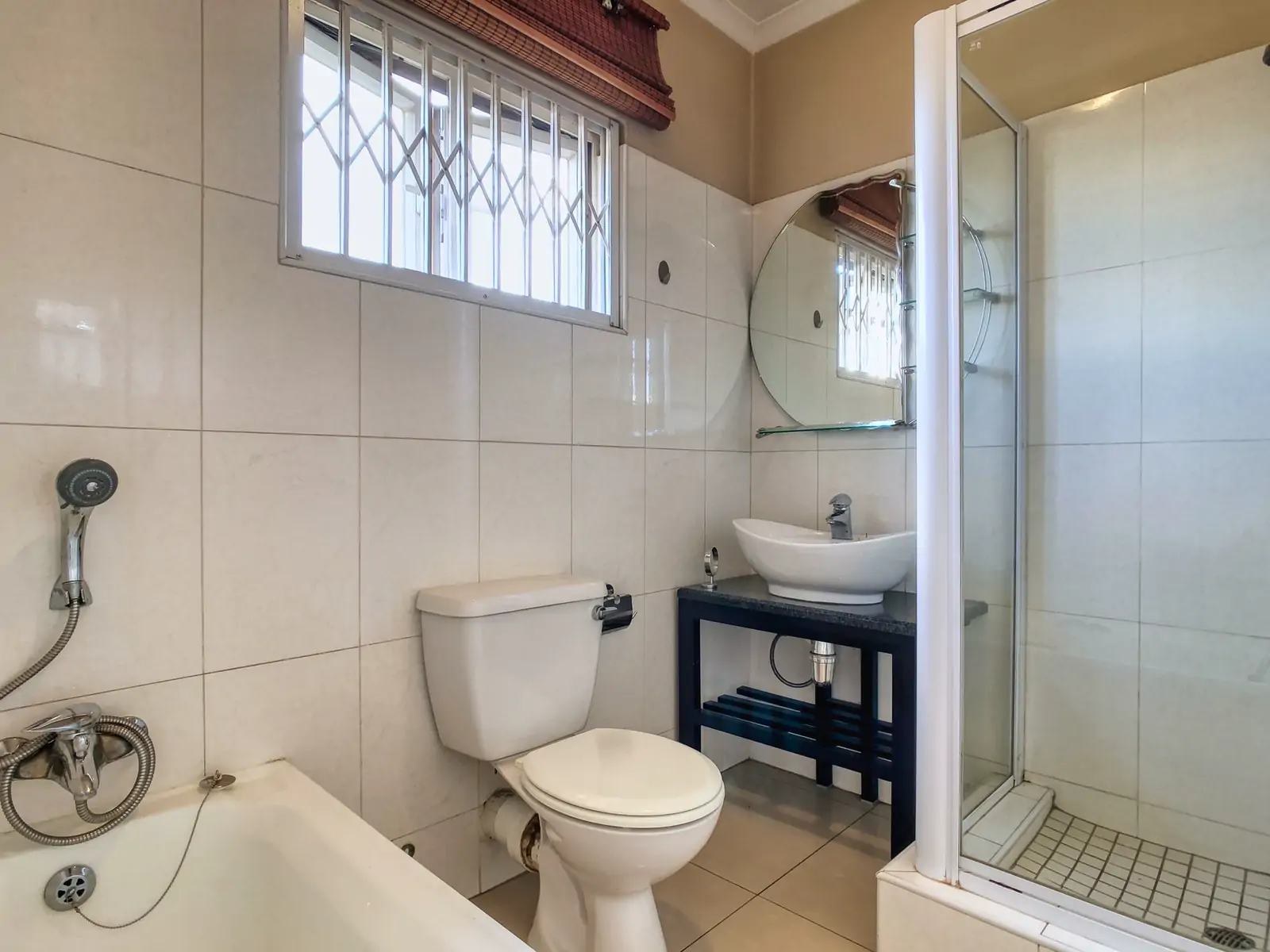 Bathroom 2: wide photo from the far corner. A bath with a hand shower, a toilet, a basin on a stand and a shower cubicle, under a window with a grille (sample photo)