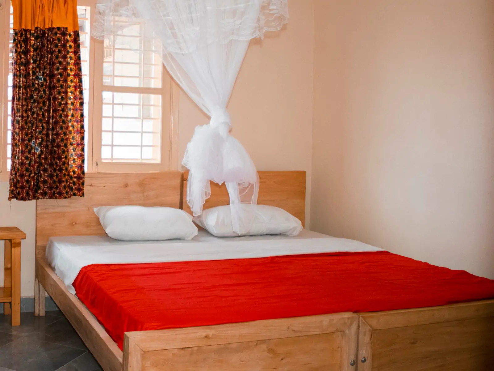 Bedroom 1: wide photo from the far corner. The bed from the window side, with two white pillows and the mosquito net tied up above it (sample photo)