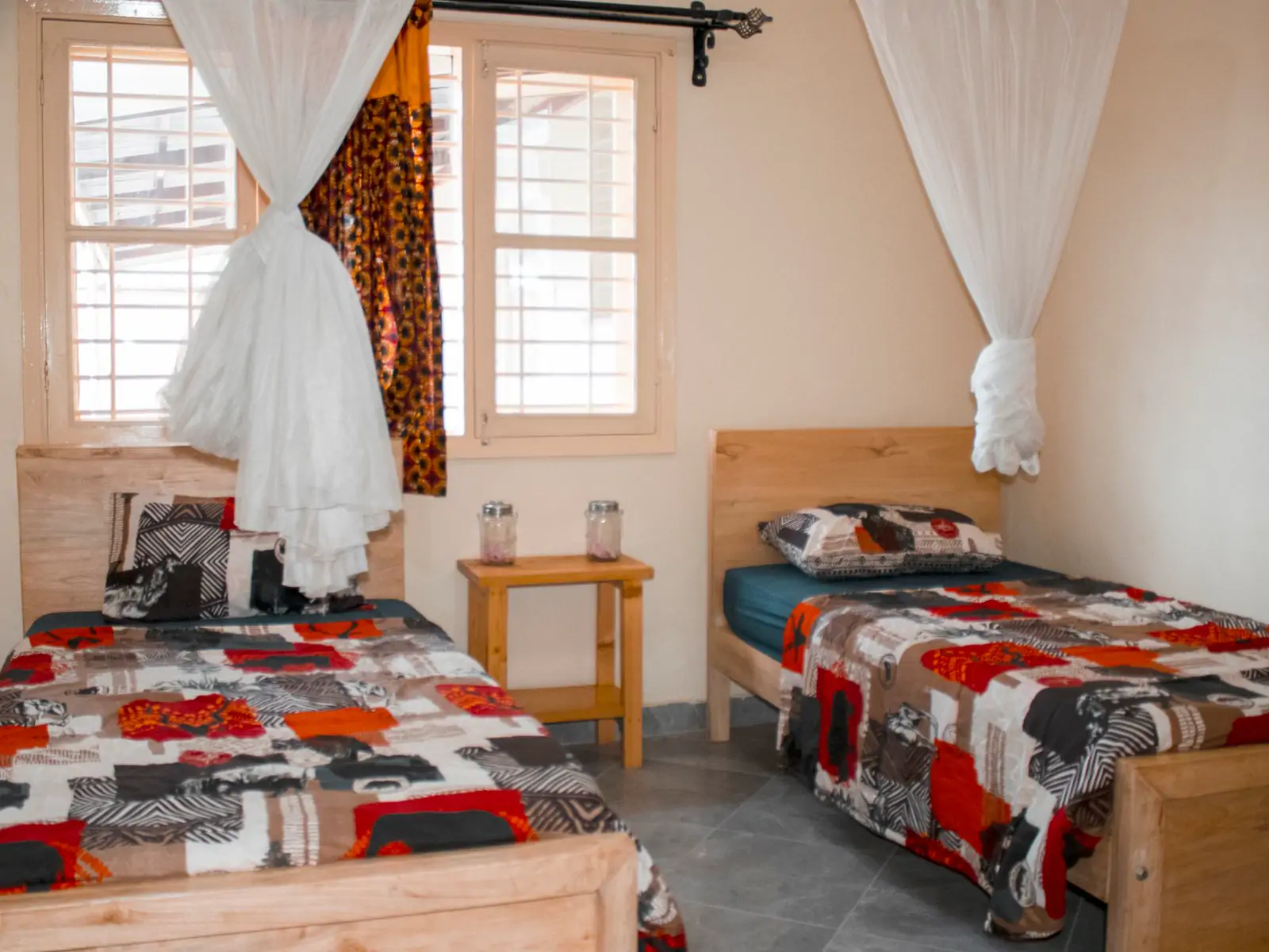 Bedroom 2: wide photo from the far corner. Two single beds with print quilts, a bedside table and two windows (sample photo)